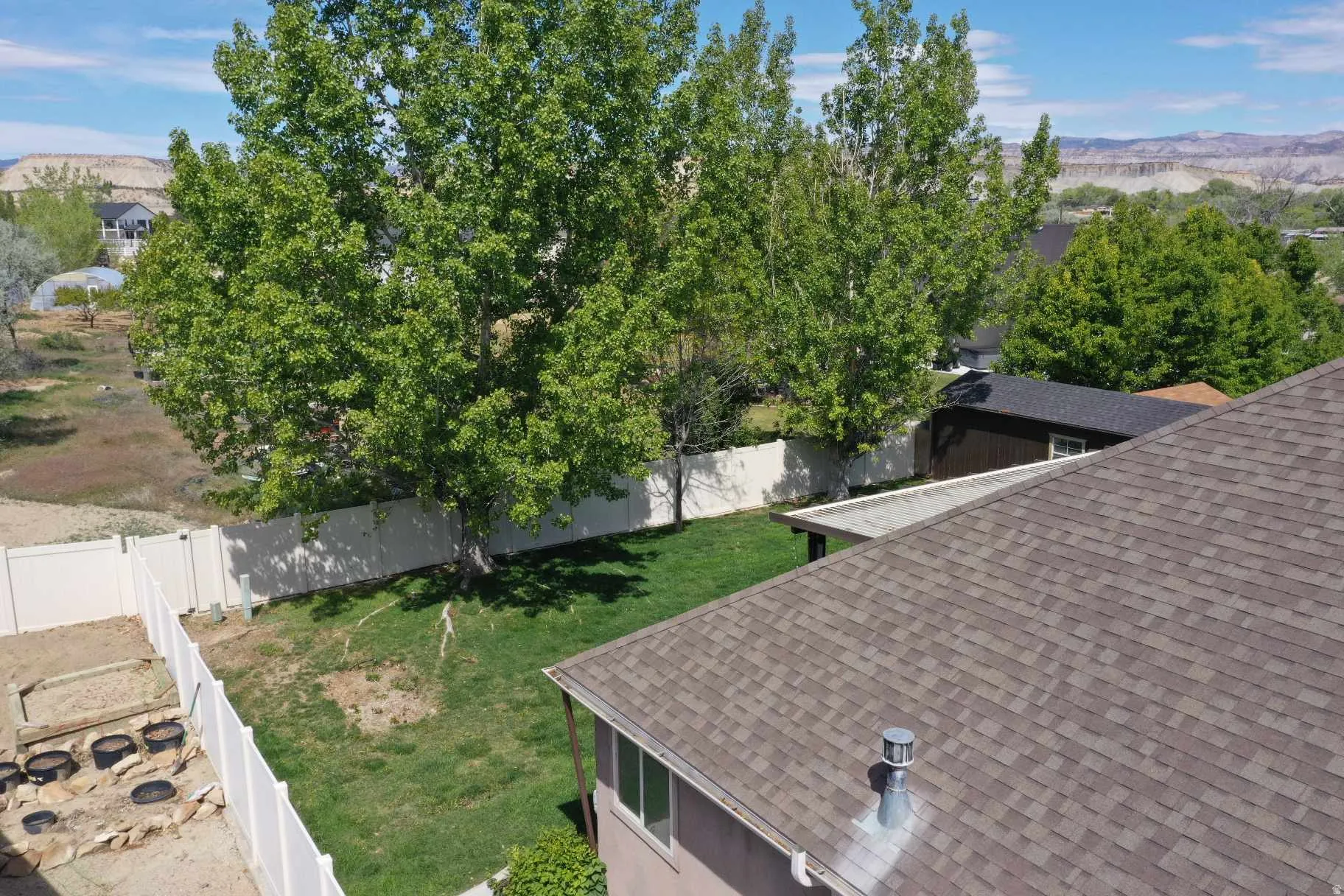 Expansive backyard featuring a green lawn, mature trees, white vinyl fencing, and a separate raised garden area