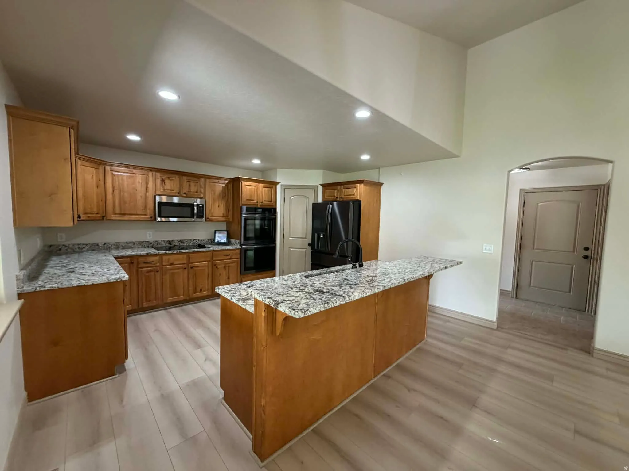 Kitchen featuring wood finish cabinets, light stone counters, black appliances, light wood finished floors, and recessed lighting