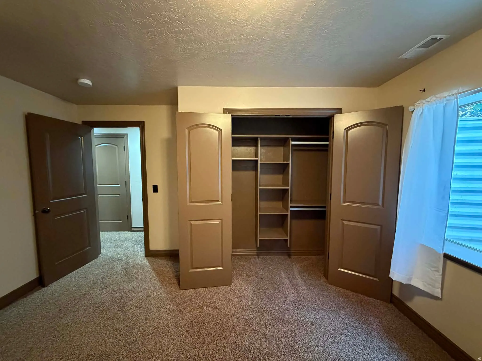 Unfurnished bedroom with light colored carpet, a textured ceiling, and a closet