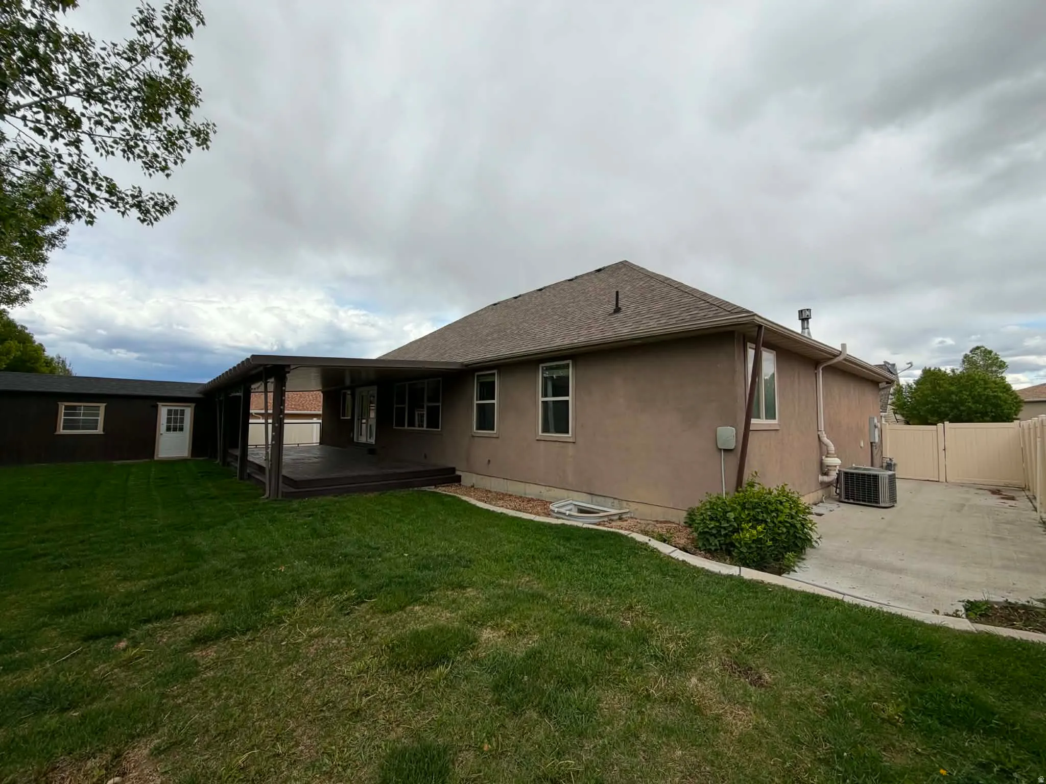 Rear view of property featuring a gate, a deck, a lawn, stucco siding, and a shingled roof