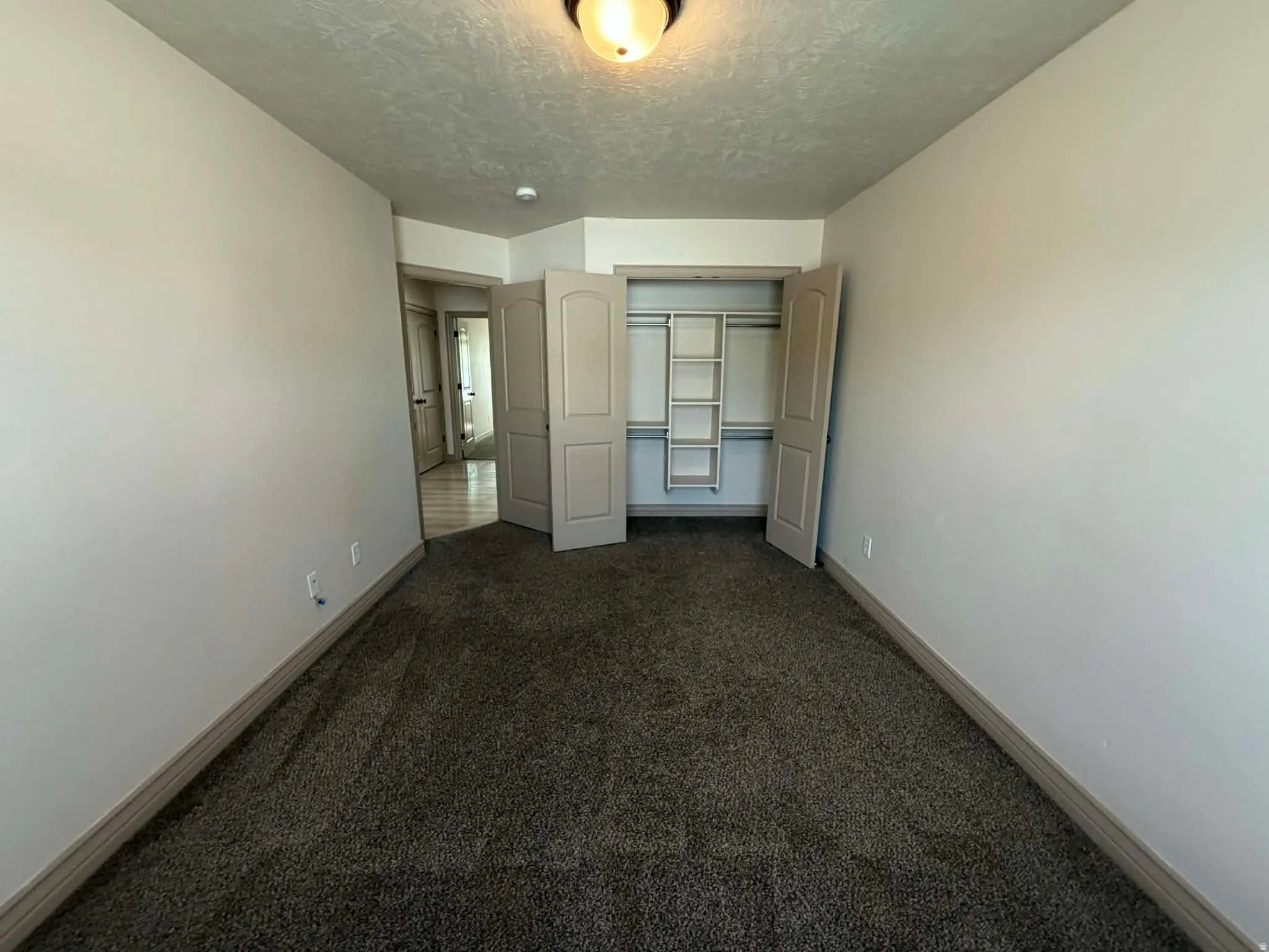 Unfurnished bedroom with dark colored carpet, a closet, and a textured ceiling