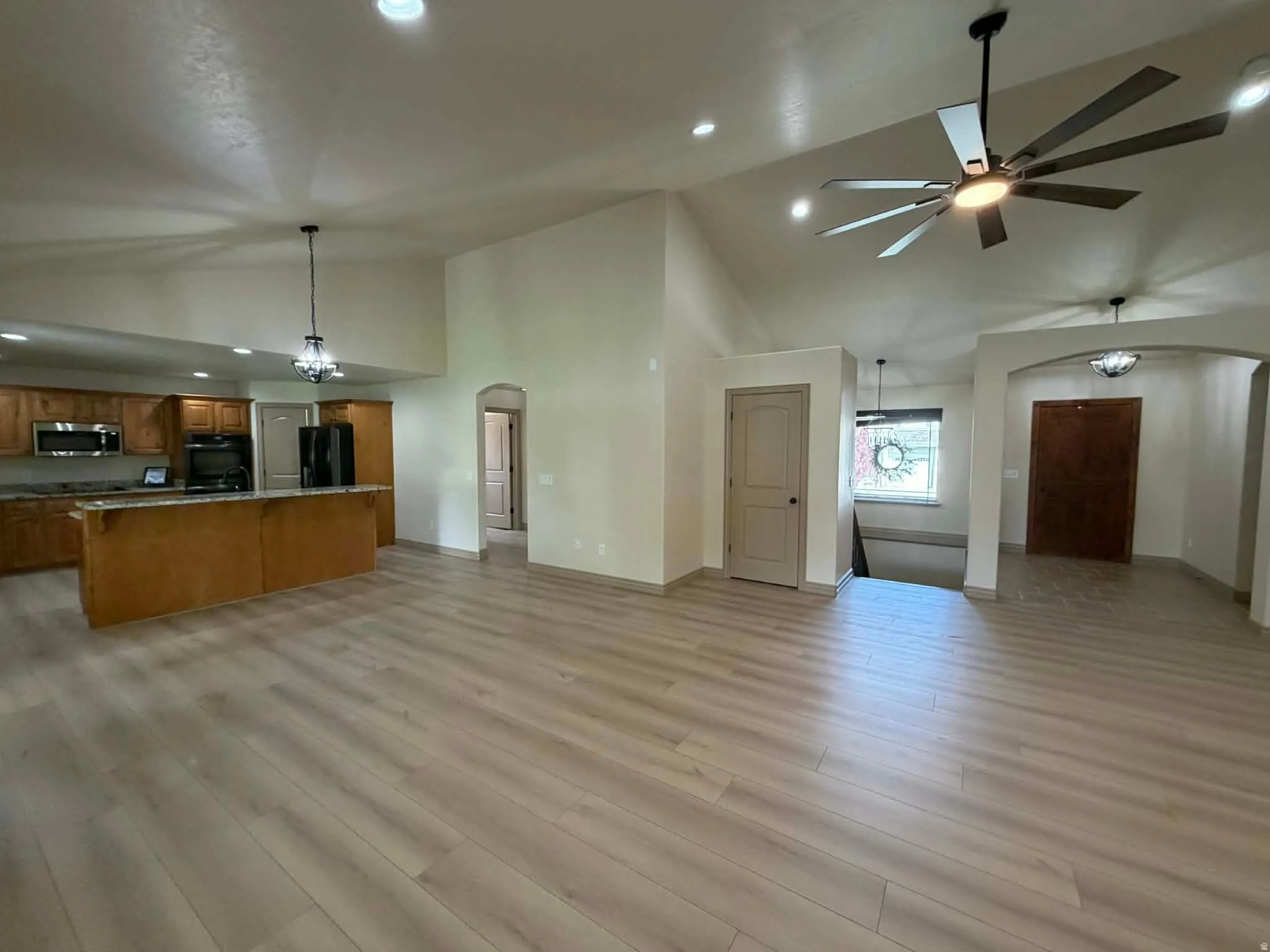 Unfurnished living room featuring arched walkways, ceiling fan, vaulted ceiling, light wood-style floors, and a chandelier
