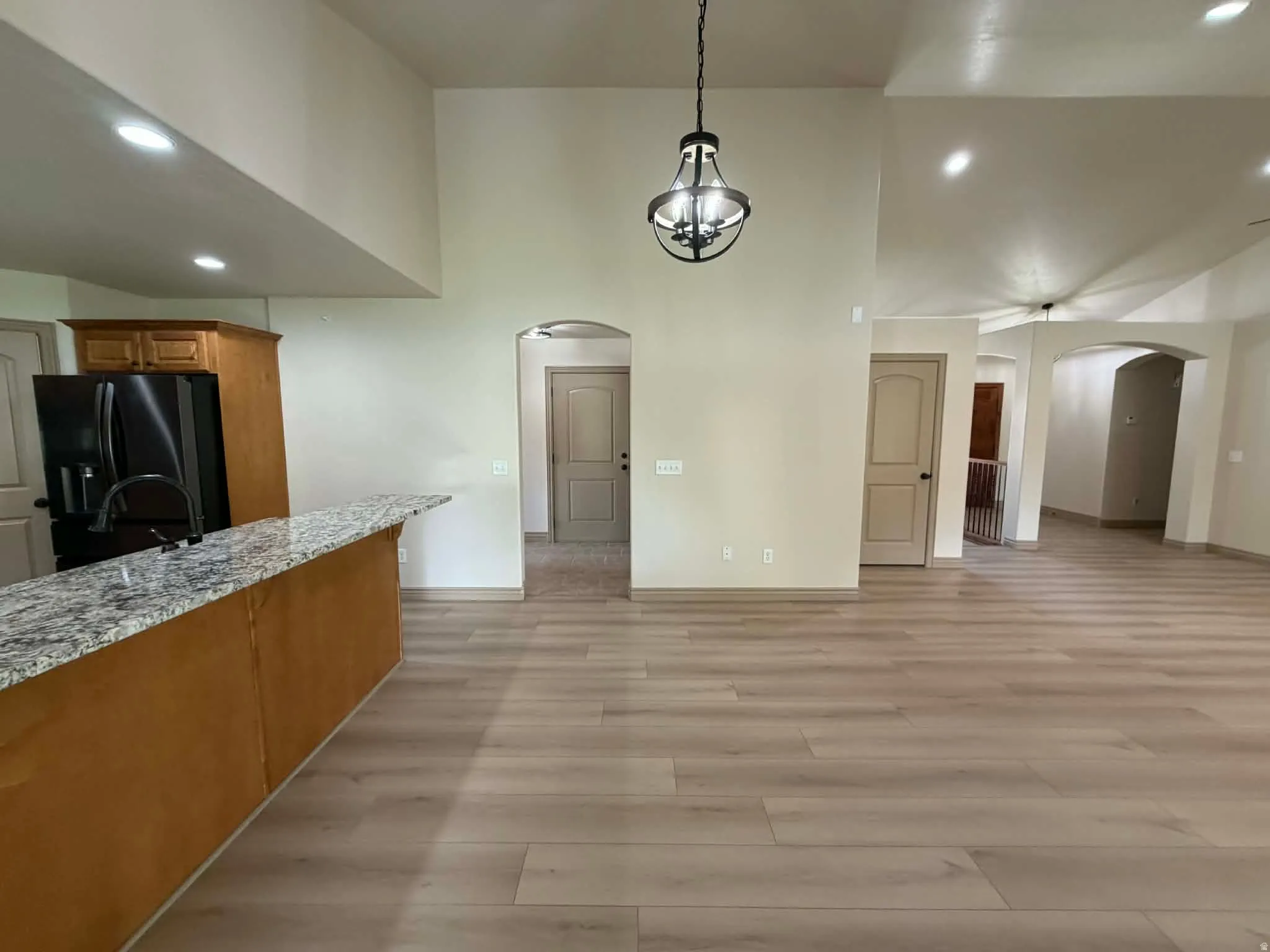 Unfurnished dining area with arched walkways, recessed lighting, light wood-type flooring, and a high ceiling