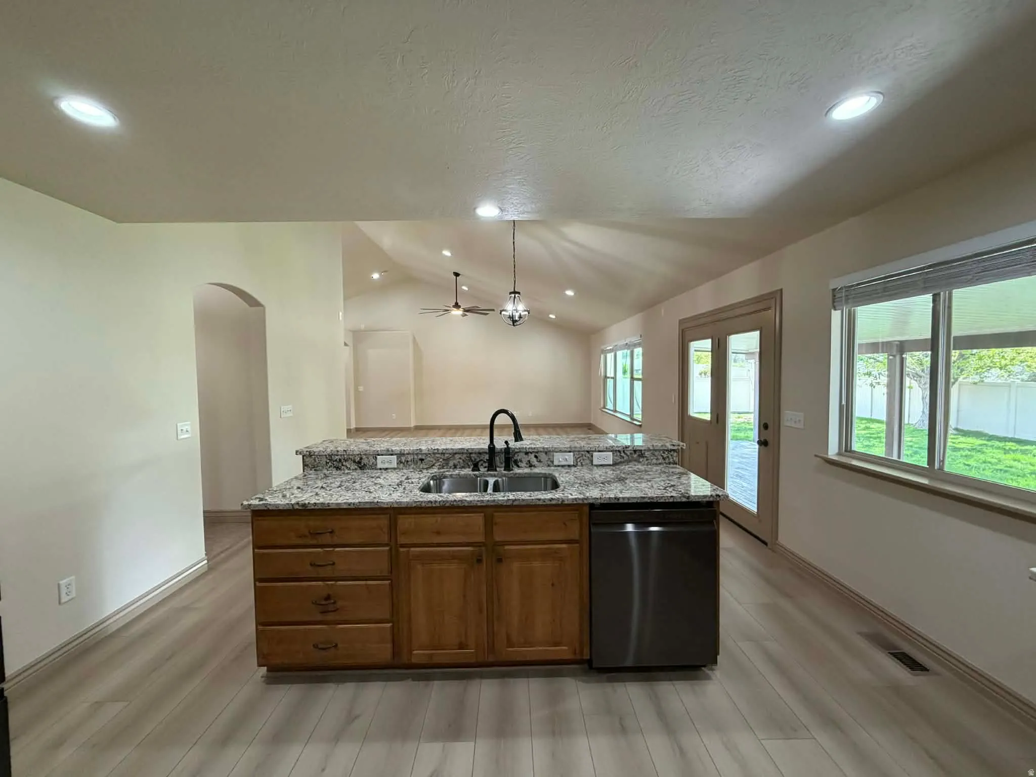 Kitchen with a kitchen island with sink, dishwasher, wood finish cabinetry, light wood-style flooring, and light stone counters