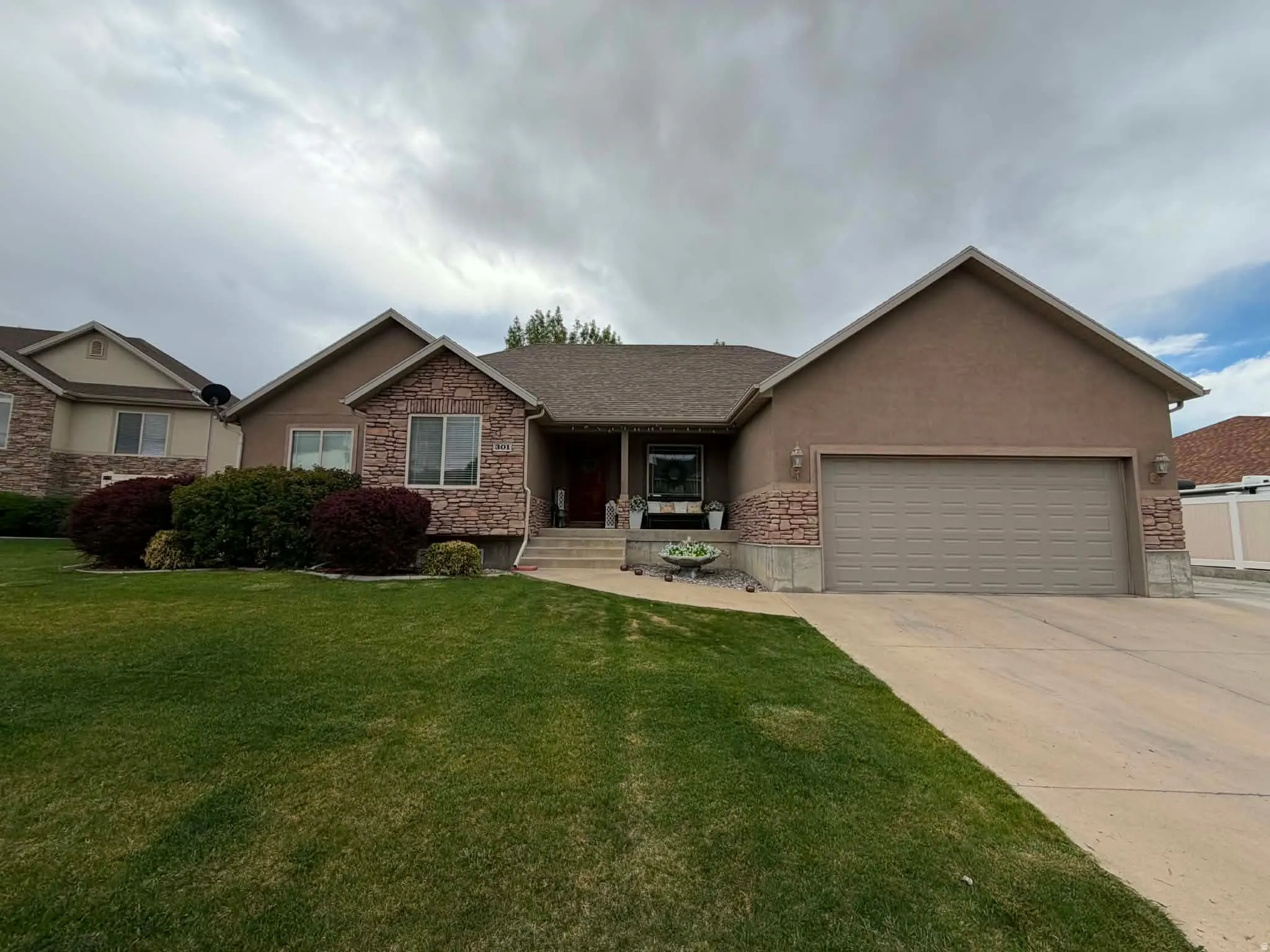 Ranch-style house featuring a porch, a garage, stone siding, concrete driveway, and stucco siding