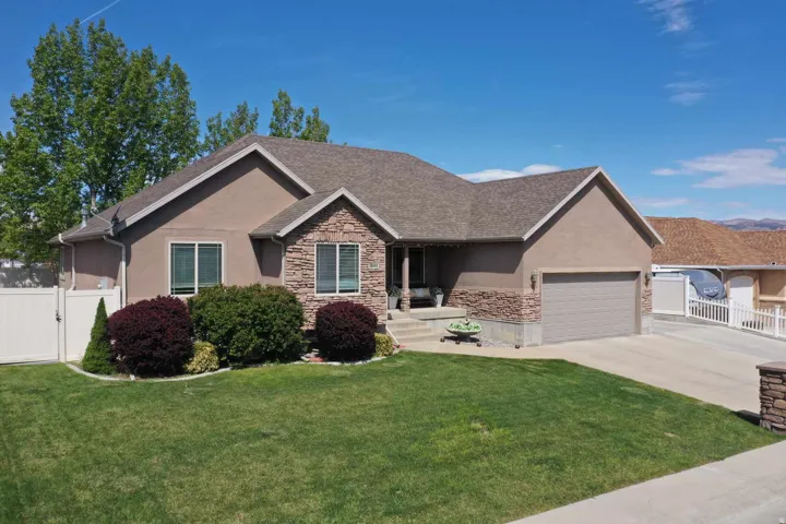 Exterior featuring stucco siding, stone accents, an attached garage, a paved driveway, and a manicured lawn