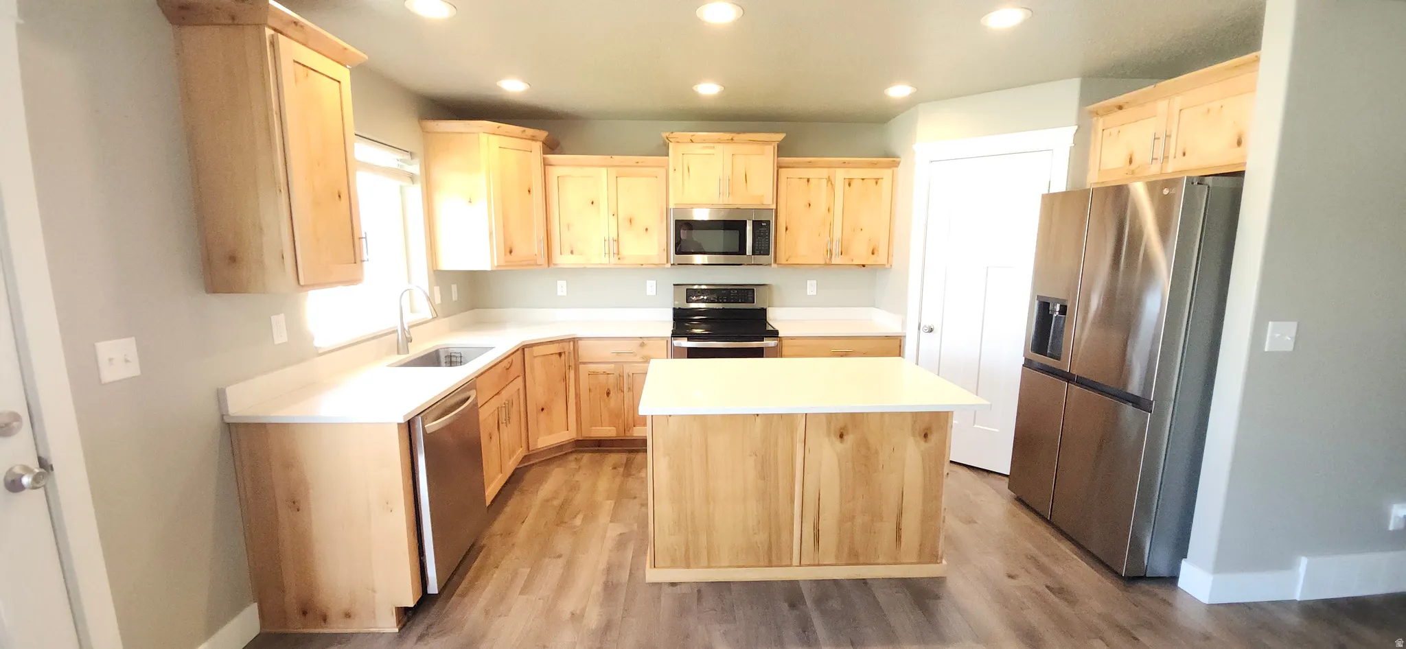 Kitchen featuring light wood finish cabinets, stainless steel appliances, light countertops, a kitchen island, and recessed lighting