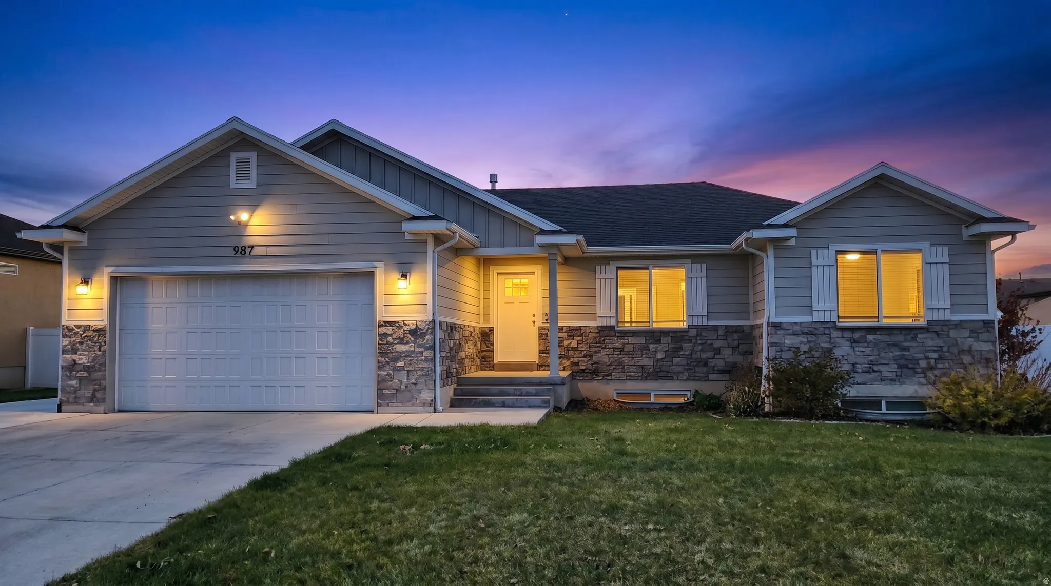 View of front of house with stone siding, a garage, concrete driveway, and a yard