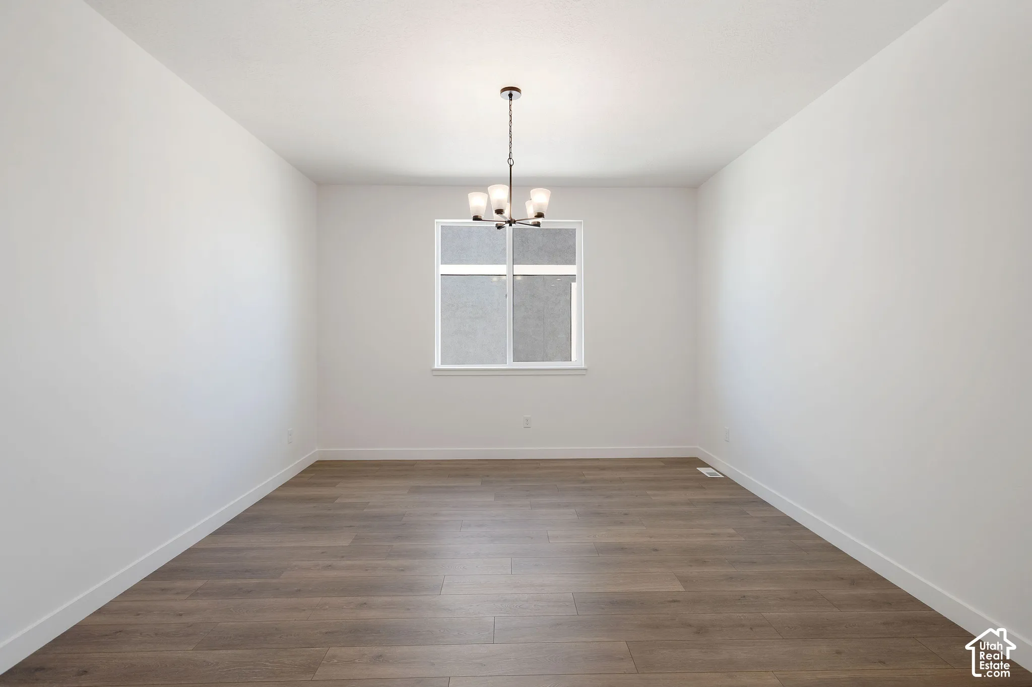 Spacious room with wood-finish flooring, white walls, and a modern chandelier