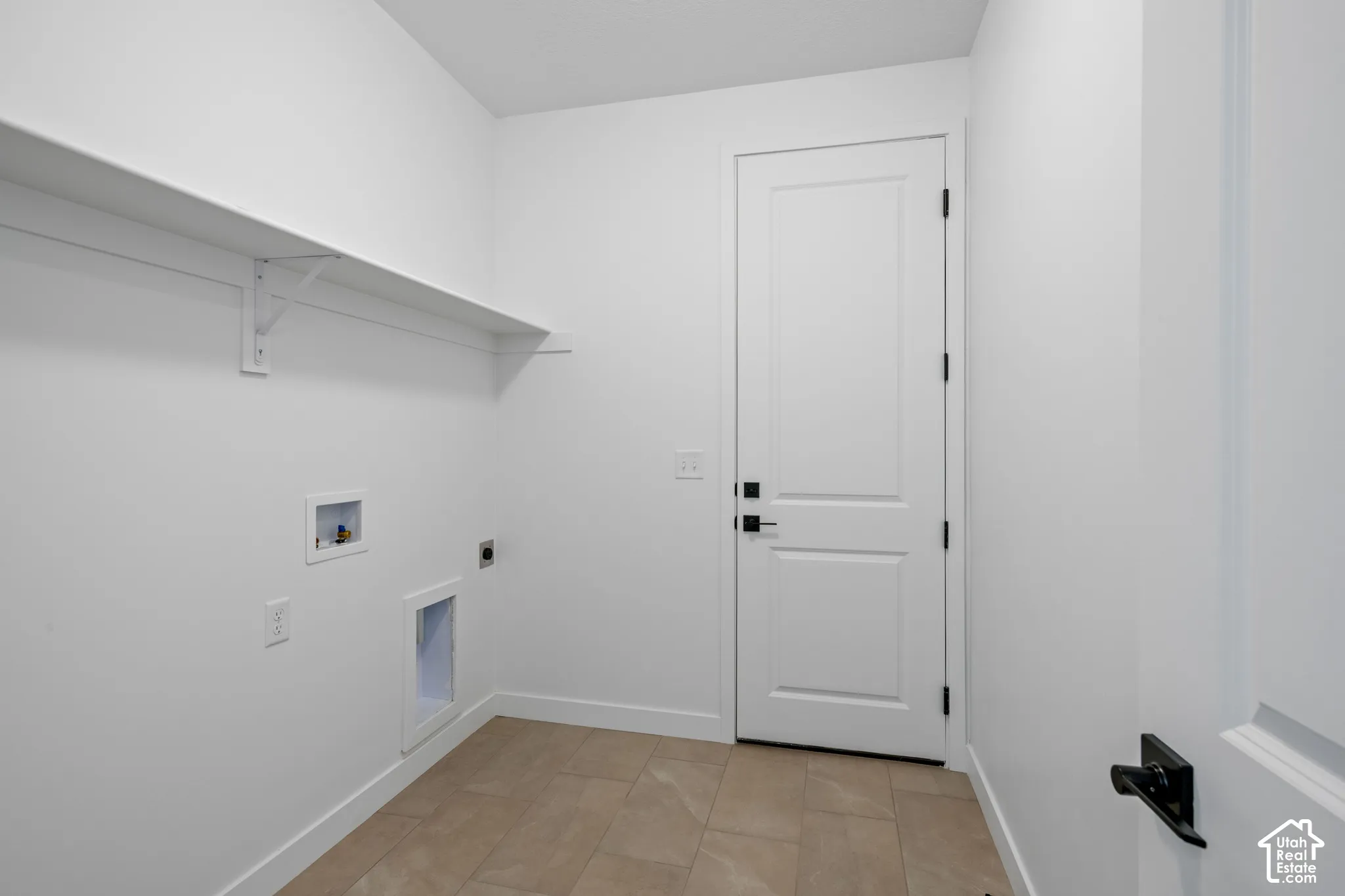 White walls featuring a single built-in shelf, tiled flooring, and a white paneled door with matte black hardware