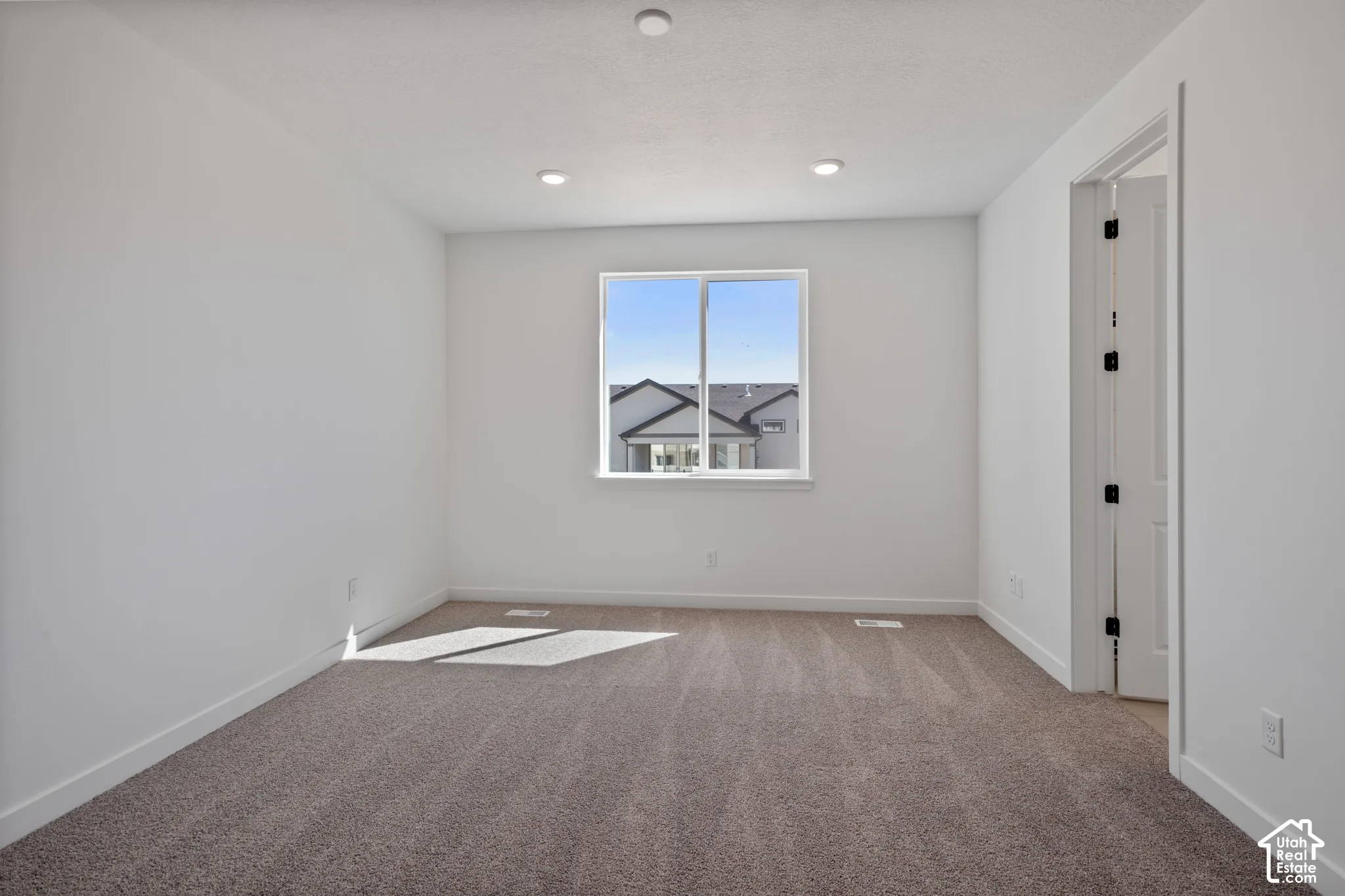 Recessed ceiling lighting, white painted walls, carpeted flooring, and a white framed window