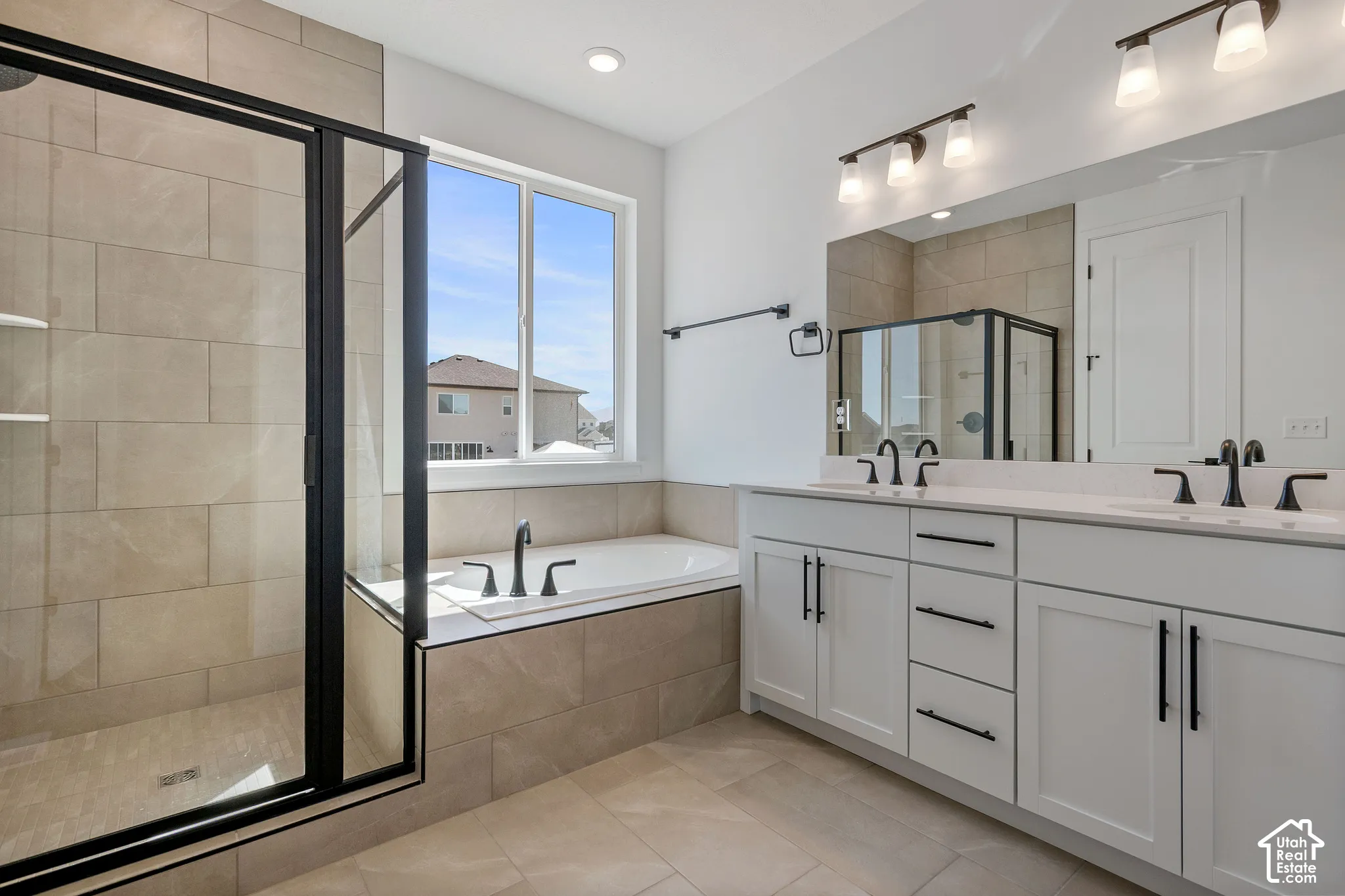 Spacious bathroom featuring a tile-surround soaking tub, walk-in shower with black-framed glass enclosure, dual vanity with white cabinetry, and matte black fixtures