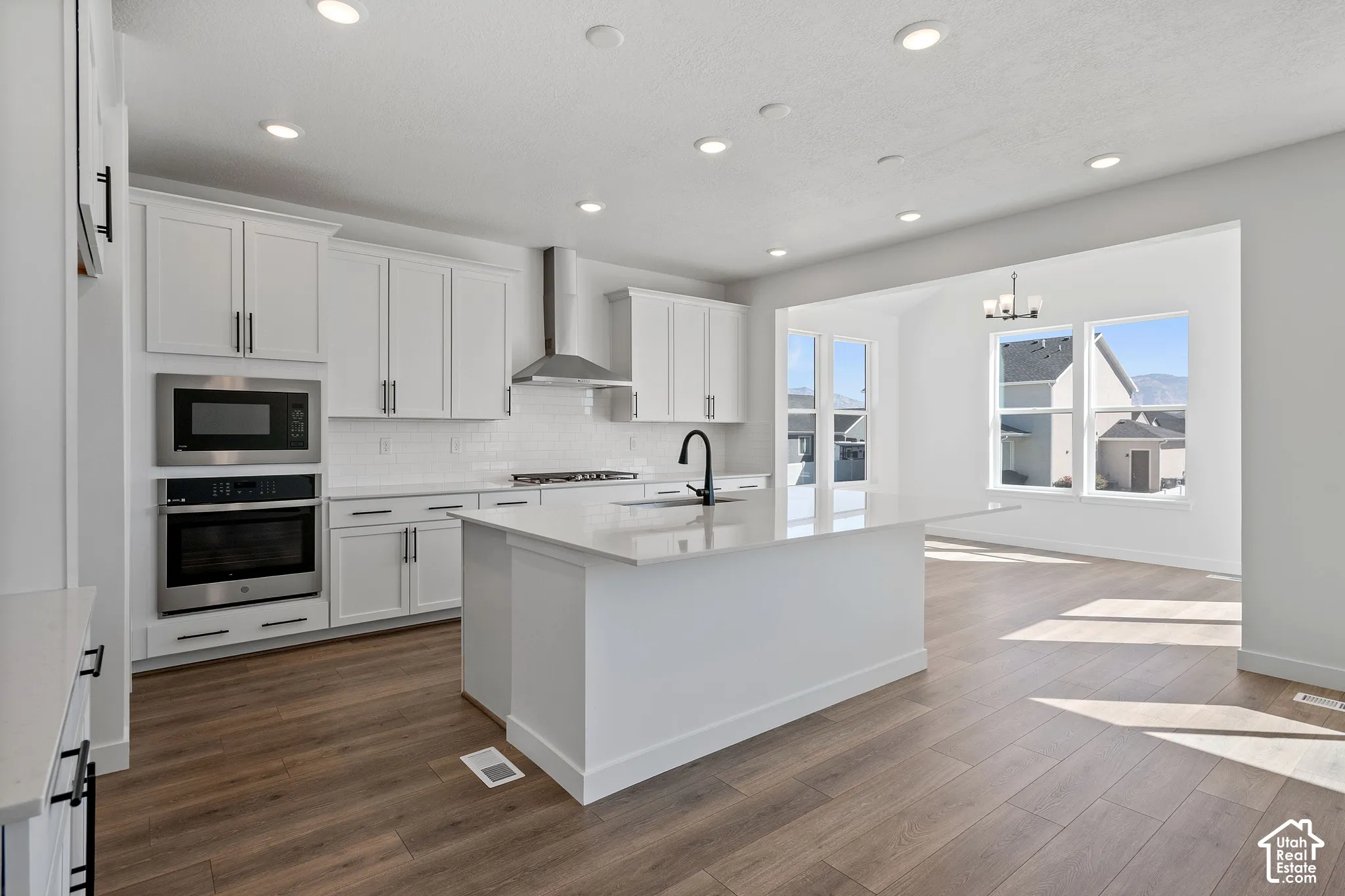 Open-concept kitchen featuring an island with a built-in sink, white cabinetry with black hardware, wood-finish flooring, and recessed lighting