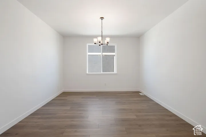 Spacious room with wood-finish flooring, white walls, and a modern chandelier
