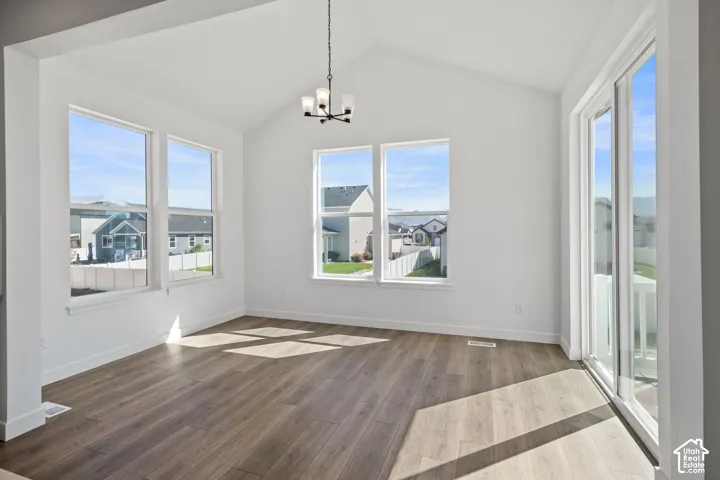 Vaulted ceiling with a chandelier, wood-finish flooring, multiple windows, and a sliding glass door