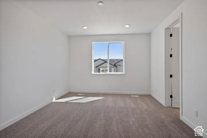 Recessed ceiling lighting, white painted walls, carpeted flooring, and a white framed window