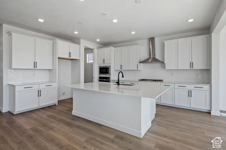 White shaker cabinetry, recessed lighting, wood-finish flooring, island with integrated sink, and subway tile backsplash
