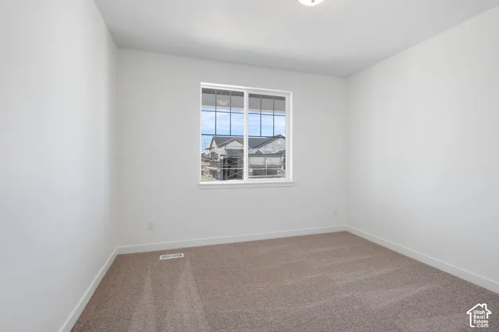 Bright interior space featuring a window with grid detailing, neutral carpeting, and white walls