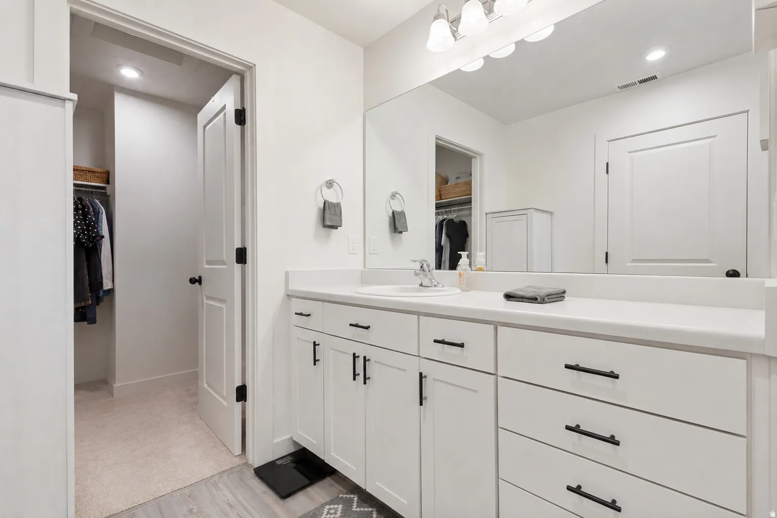 Bathroom featuring a single vanity with white cabinetry, a solid surface countertop, an undermount sink, and a large mirror