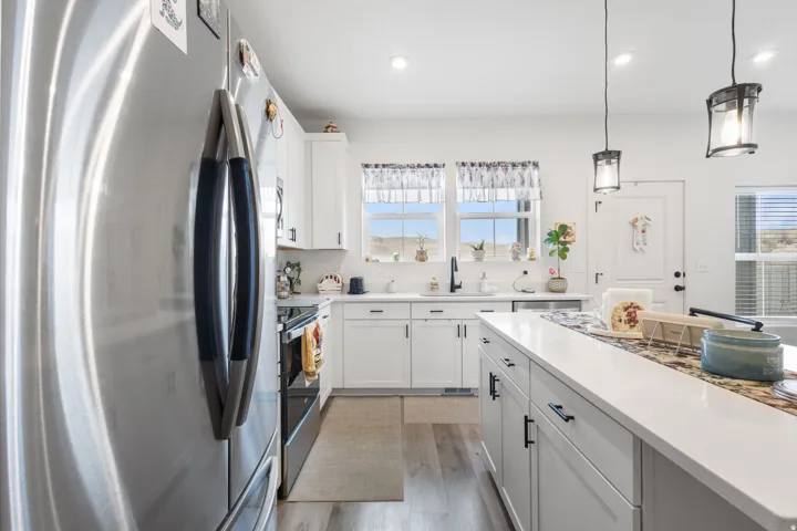 Kitchen with stainless steel appliances, white cabinets, decorative light fixtures, light wood-type flooring, and light stone counters