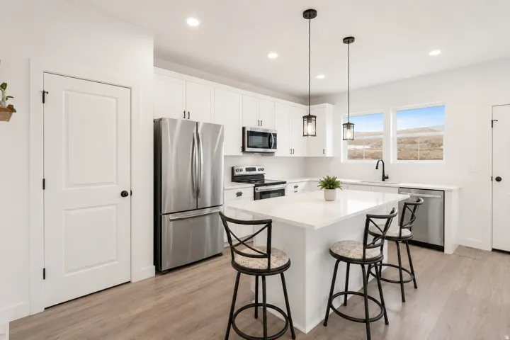 Modern kitchen featuring white cabinetry, a central island with countertop seating, stainless steel appliances, and wood-finish flooring