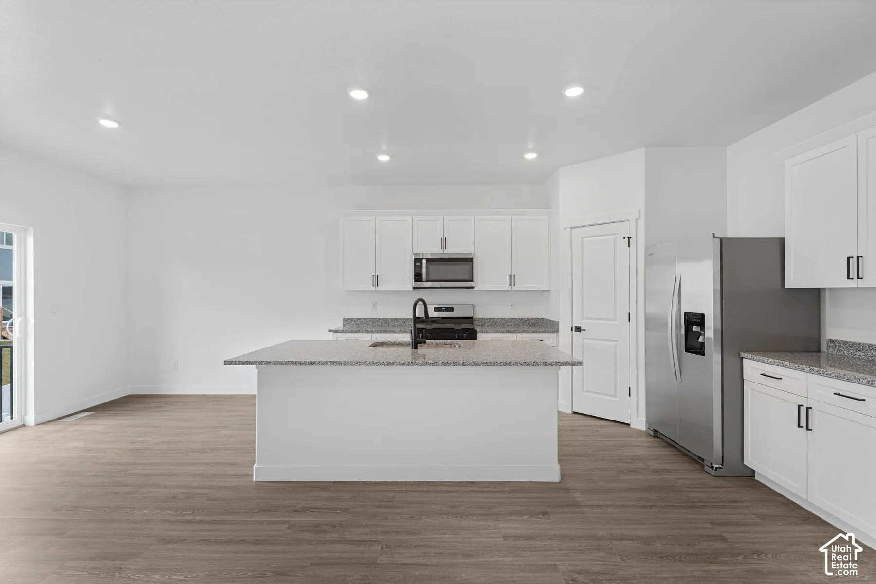 Kitchen featuring light stone countertops, white cabinetry, stainless steel appliances, recessed lighting, and light wood-type flooring