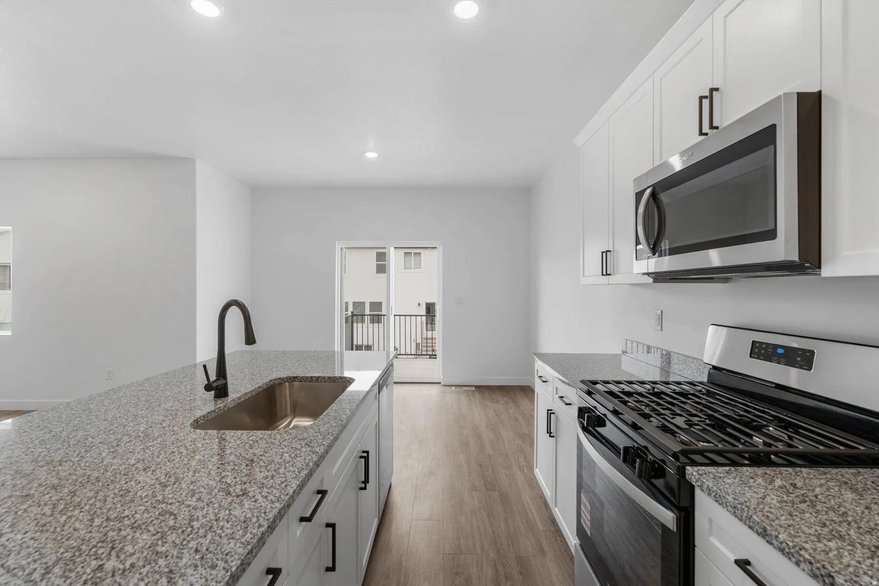 Kitchen featuring stainless steel appliances, white cabinetry, light stone countertops, light wood-style flooring, and recessed lighting