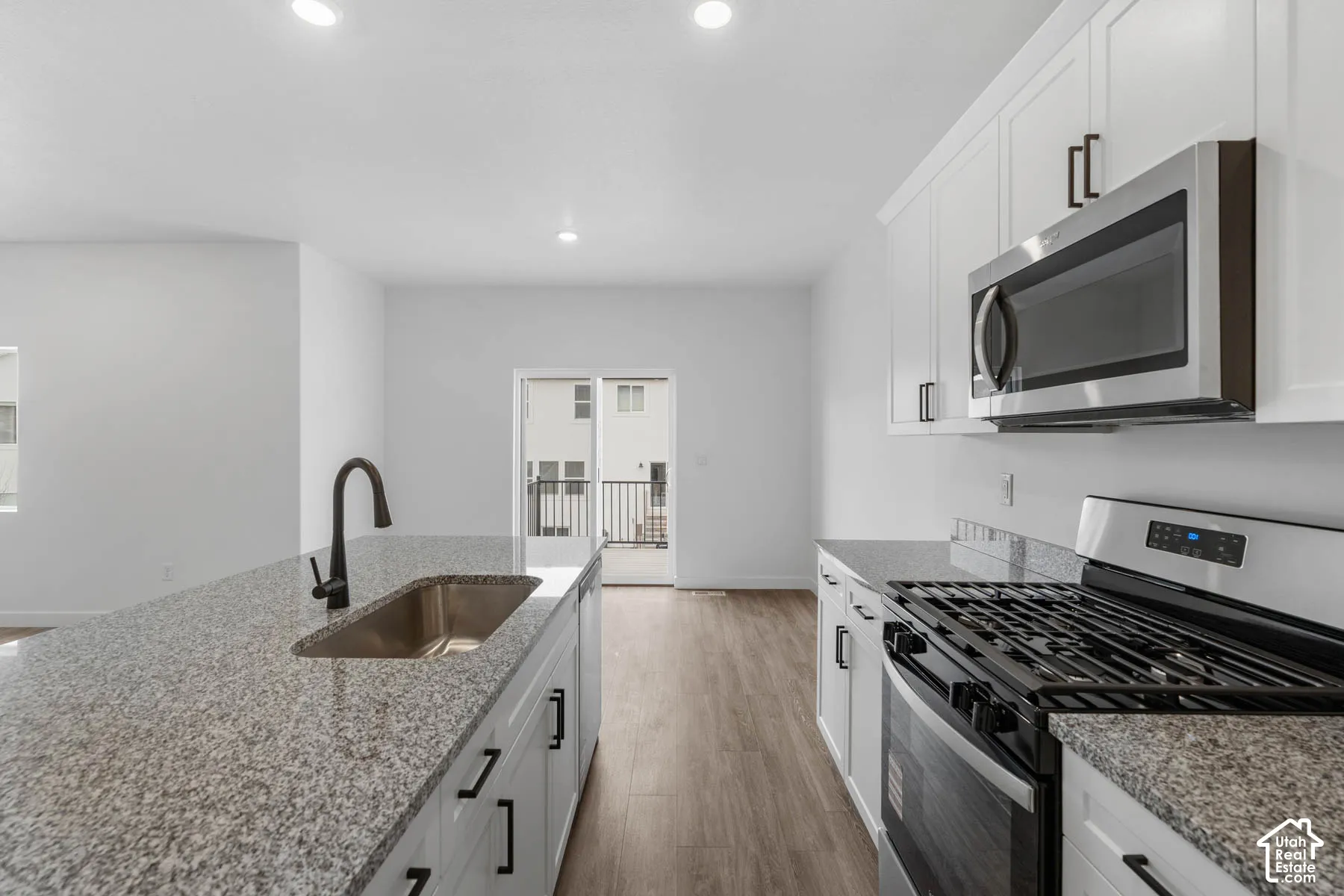 Kitchen featuring stainless steel appliances, white cabinetry, light stone countertops, light wood-style flooring, and recessed lighting