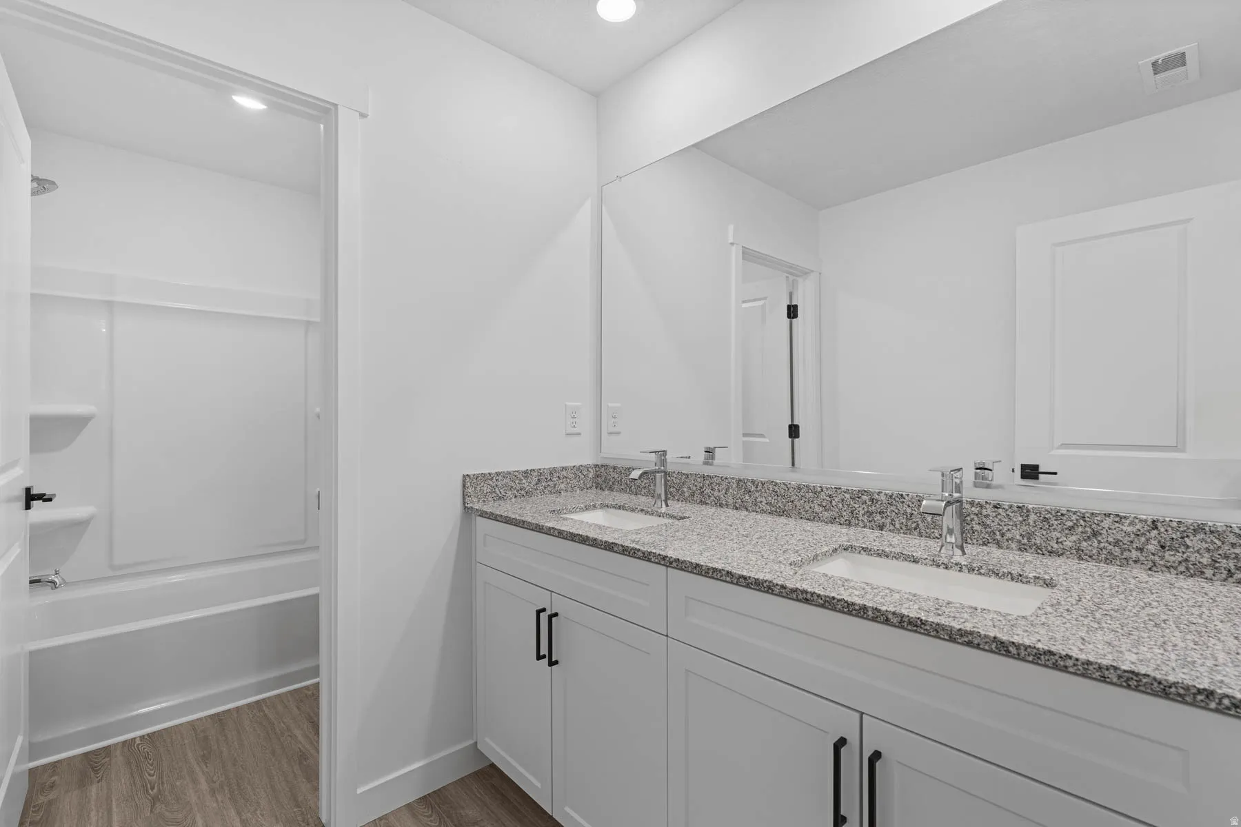 Full bath with double vanity, light wood-style flooring, recessed lighting, and shower / bath combination