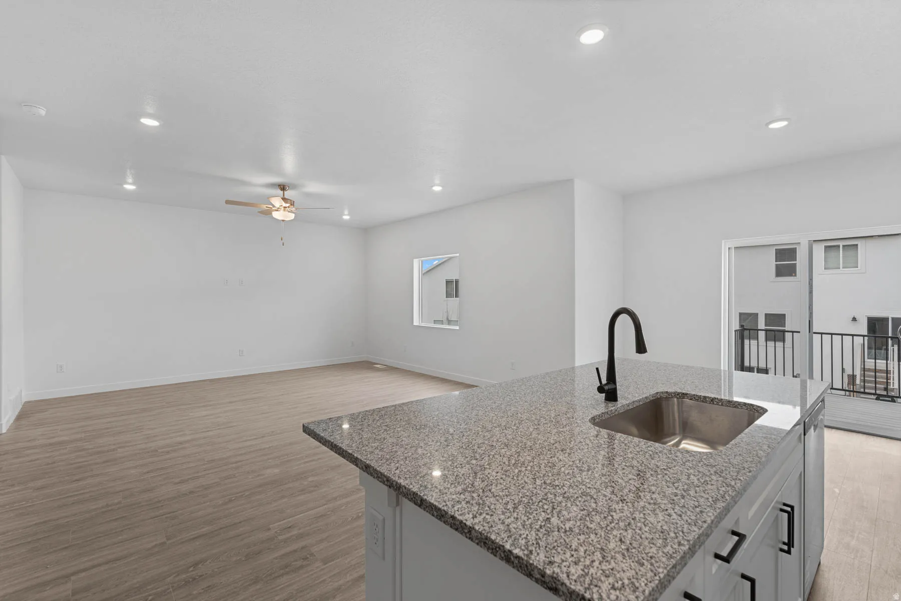 Kitchen featuring light stone counters, light wood finished floors, a kitchen island with sink, open floor plan, and recessed lighting