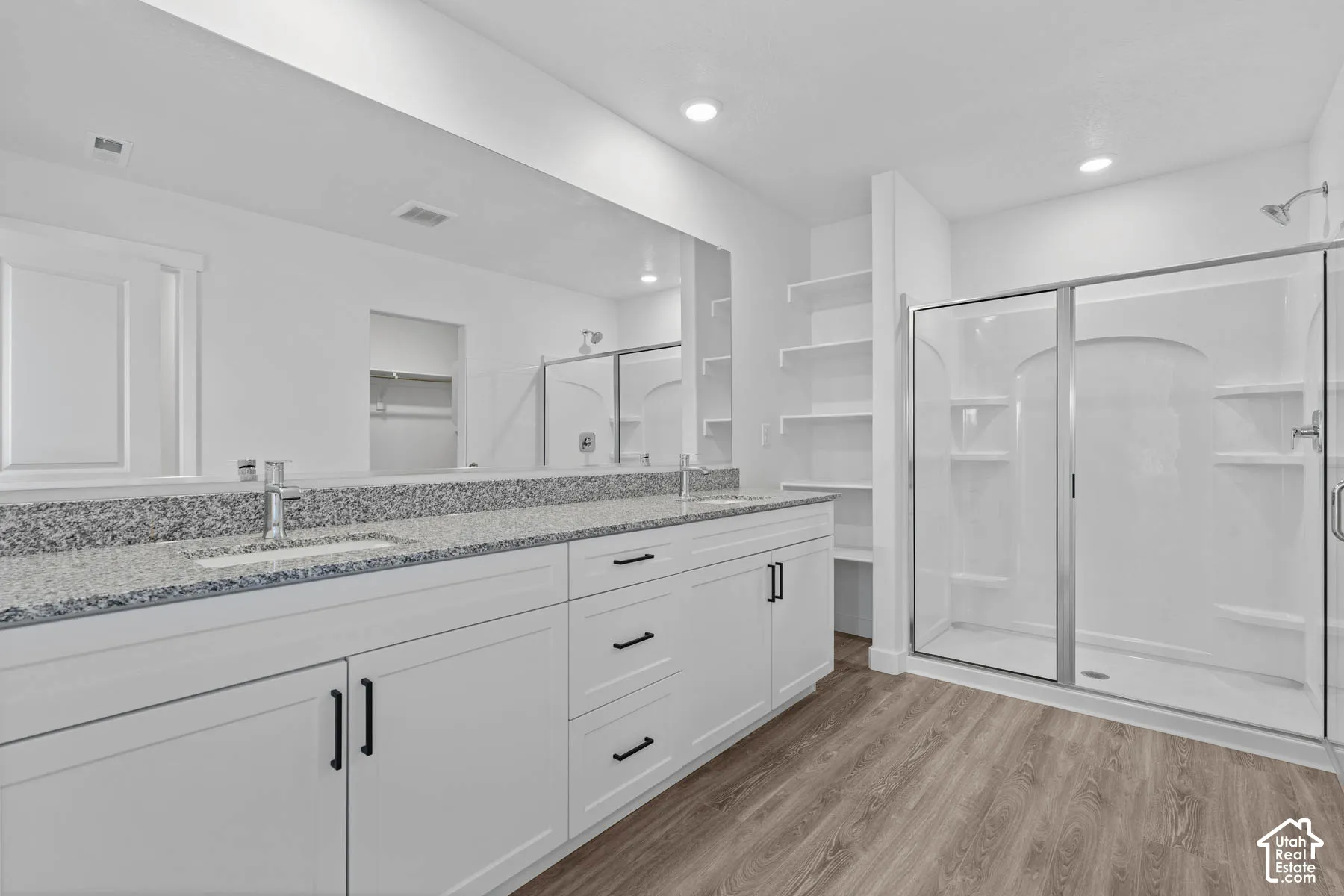 Bathroom with a shower stall, double vanity, light wood-style floors, a spacious closet, and recessed lighting