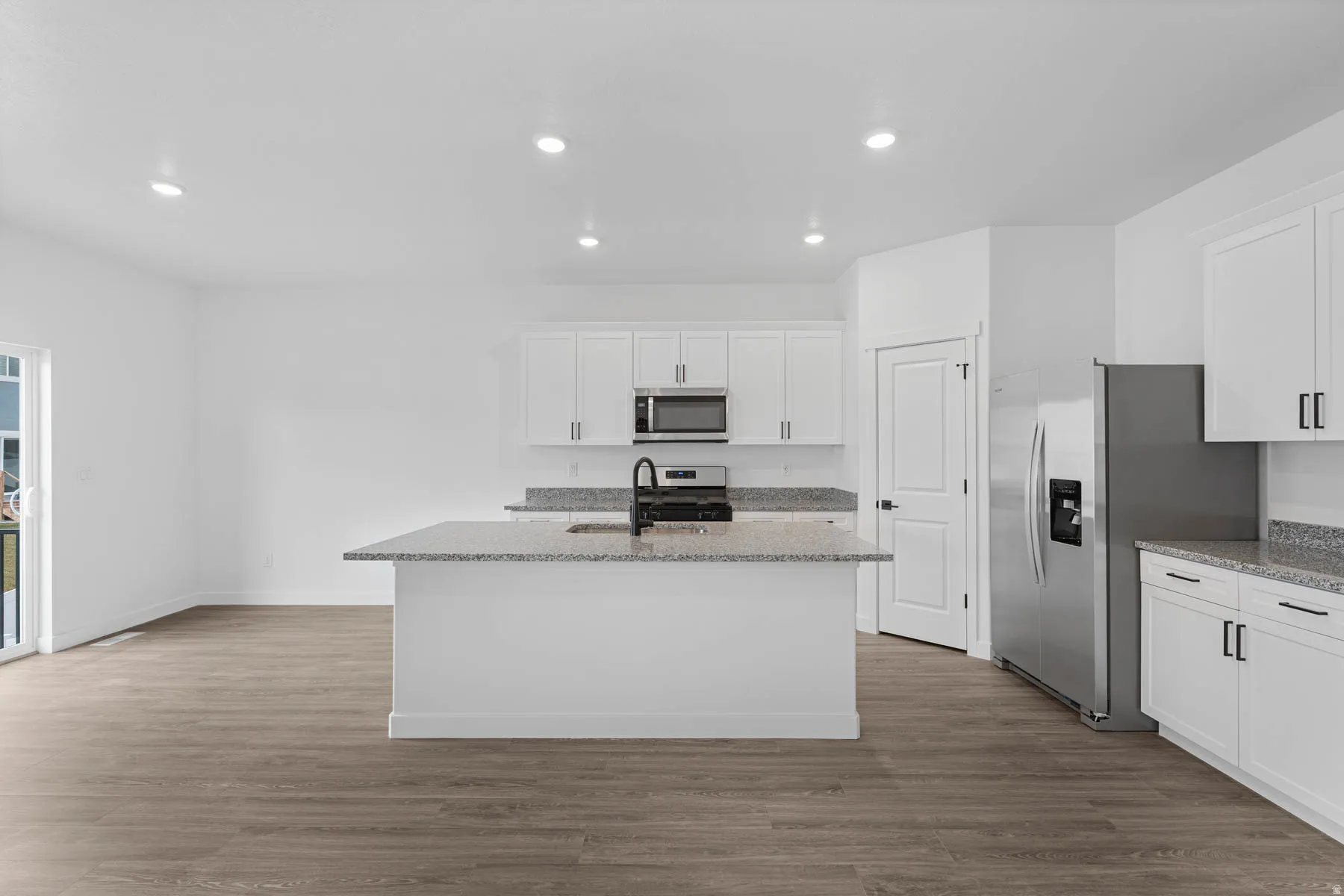 Kitchen featuring light stone countertops, white cabinetry, stainless steel appliances, recessed lighting, and light wood-type flooring