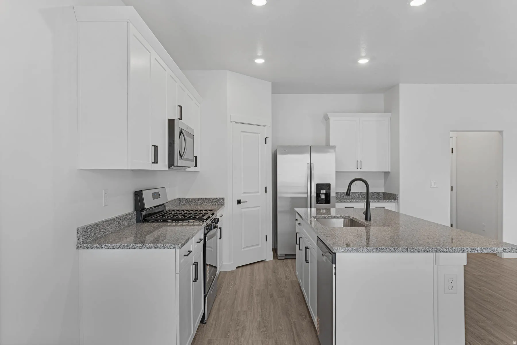 Kitchen with stainless steel appliances, light wood-style flooring, light stone countertops, white cabinetry, and recessed lighting