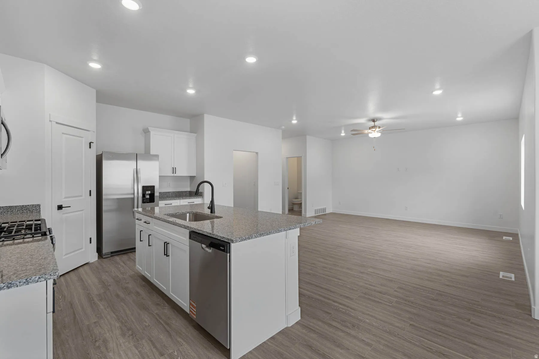 Kitchen featuring stainless steel appliances, white cabinets, a kitchen island with sink, recessed lighting, and light stone counters