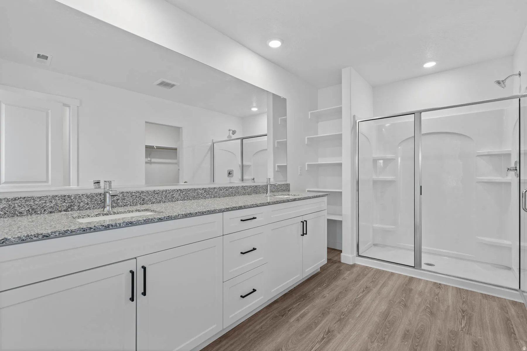 Bathroom with a shower stall, double vanity, light wood-style floors, a spacious closet, and recessed lighting