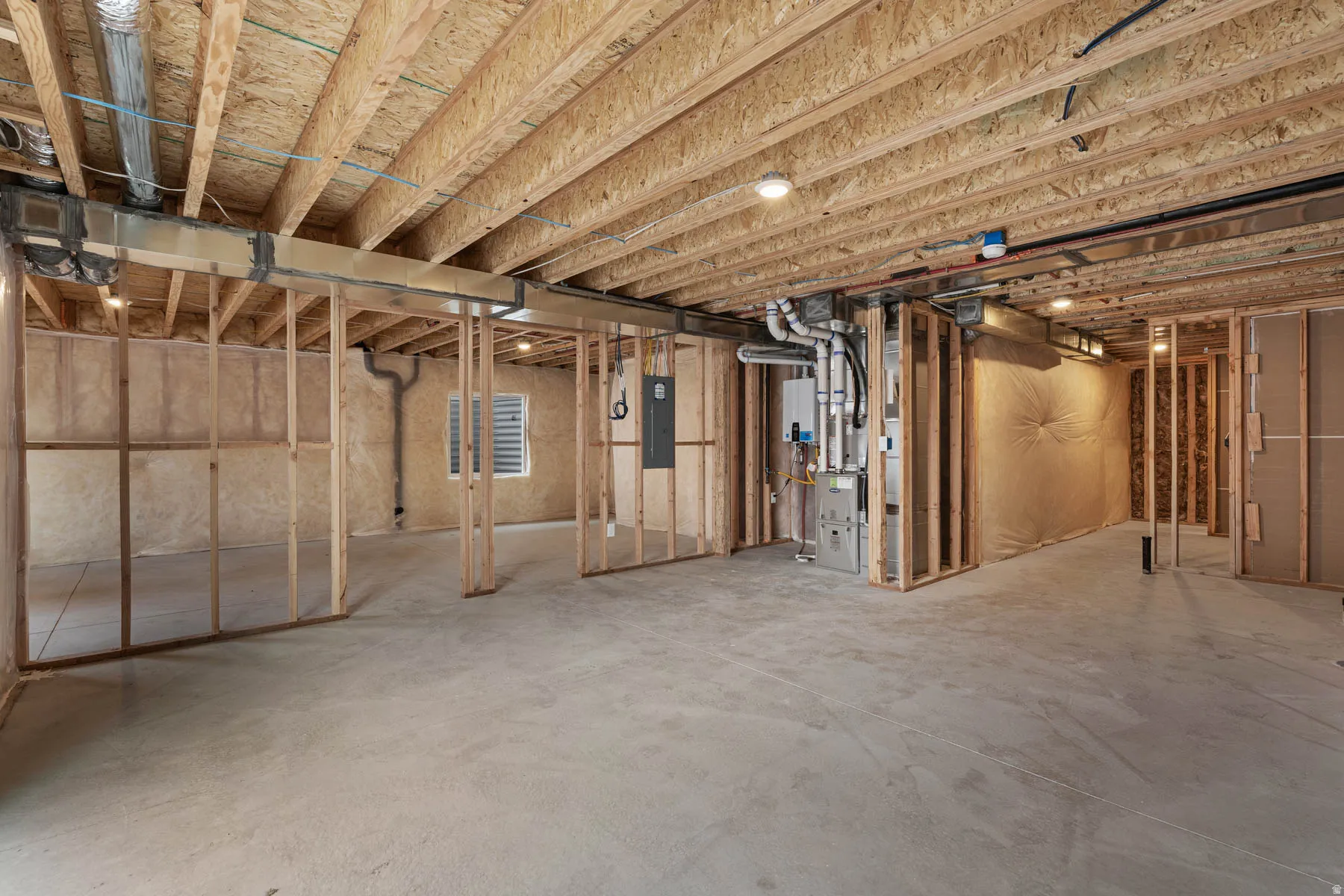Unfinished below grade area featuring heating unit, electric panel, and tankless water heater