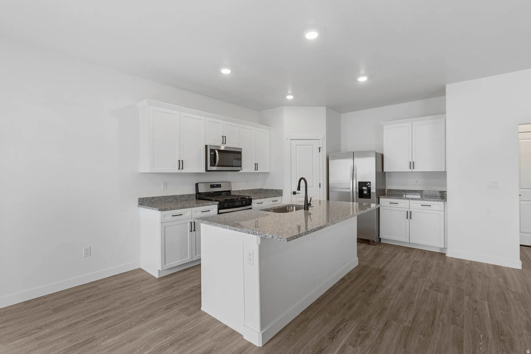 Kitchen with light wood finished floors, stainless steel appliances, light stone counters, white cabinetry, and recessed lighting