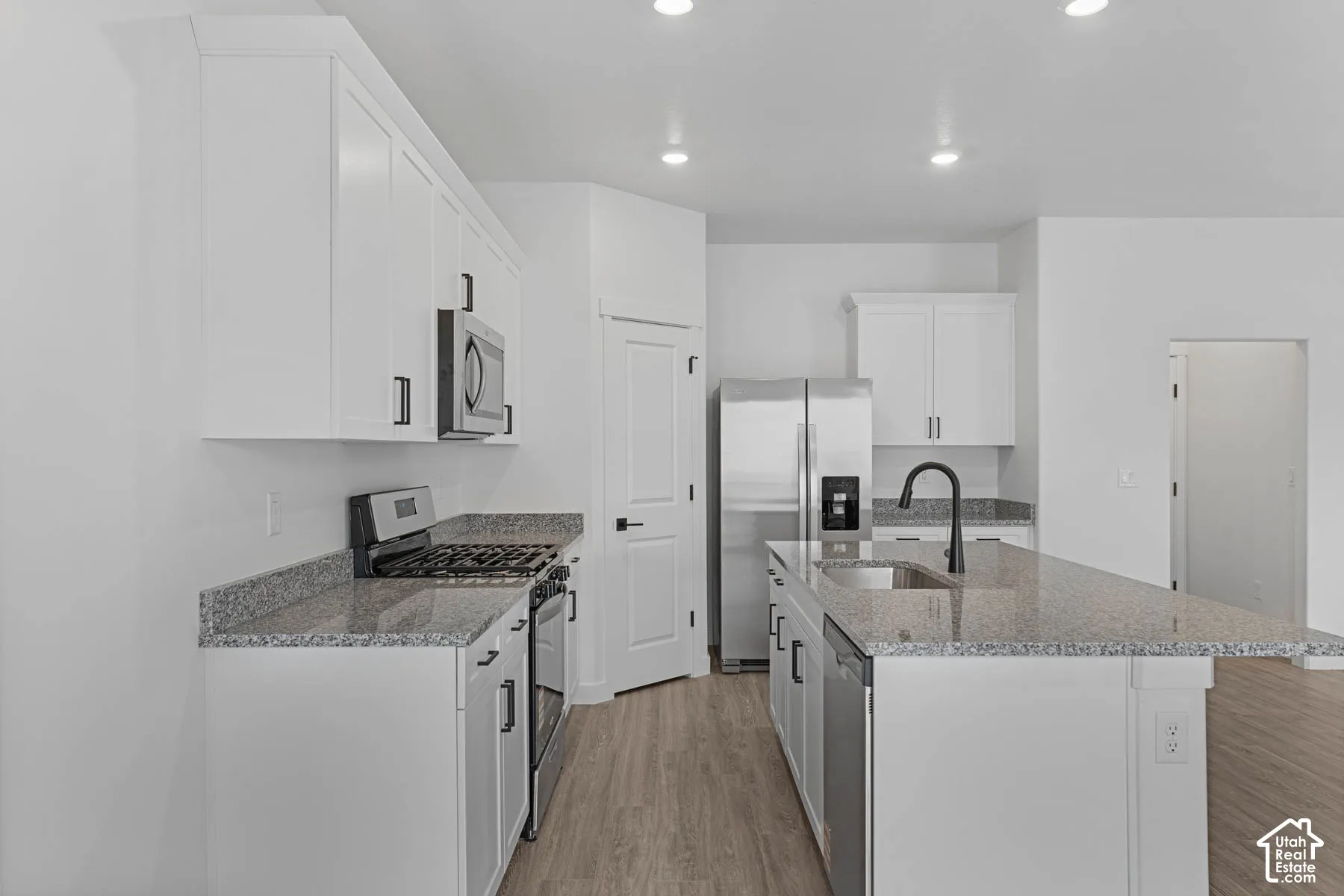 Kitchen with stainless steel appliances, light wood-style flooring, light stone countertops, white cabinetry, and recessed lighting