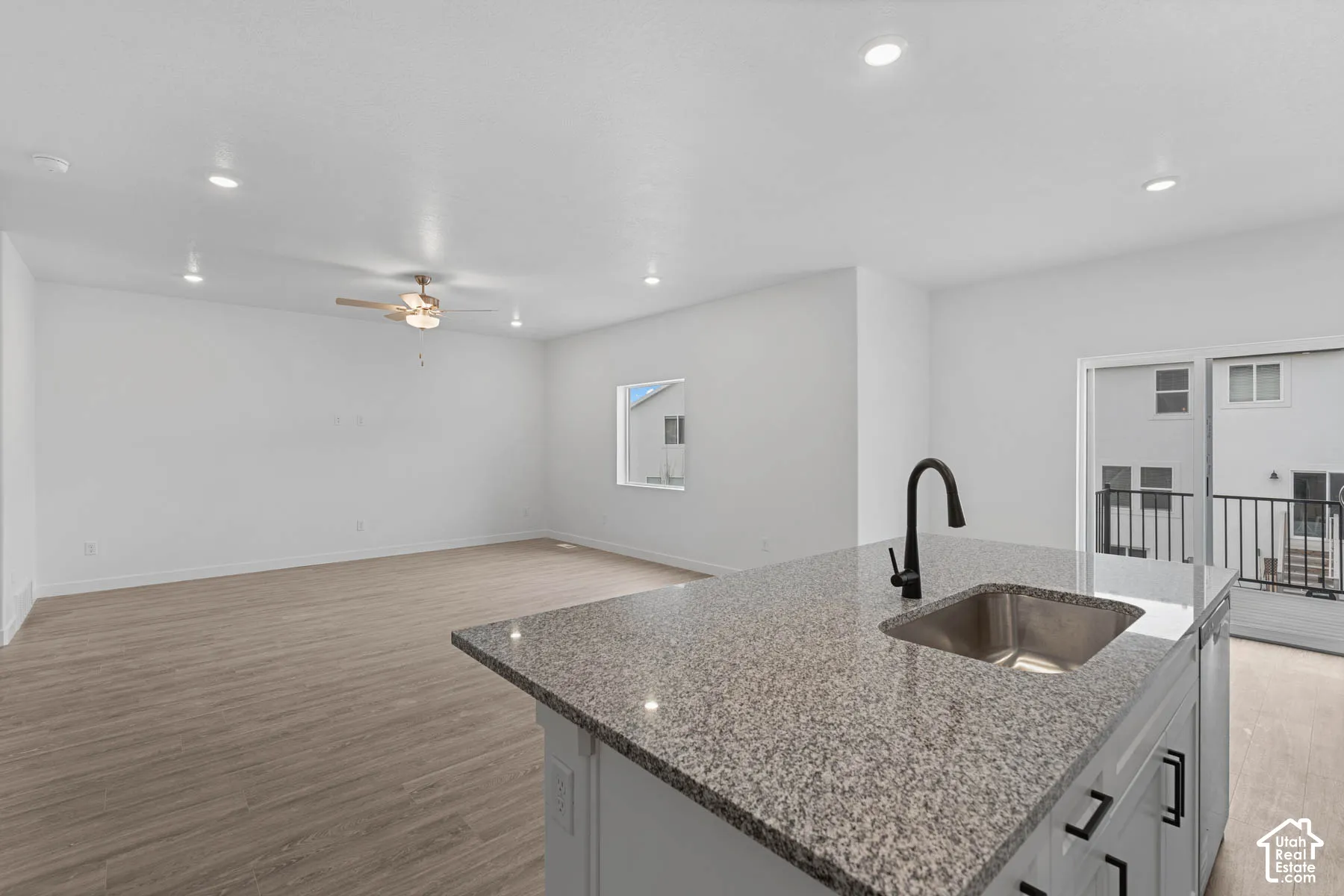 Kitchen featuring light stone counters, light wood finished floors, a kitchen island with sink, open floor plan, and recessed lighting