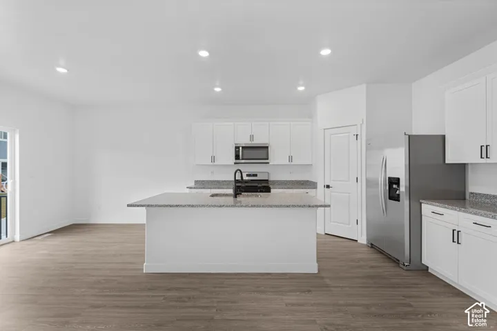Kitchen featuring light stone countertops, white cabinetry, stainless steel appliances, recessed lighting, and light wood-type flooring