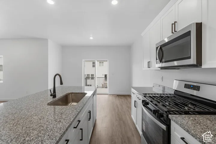 Kitchen featuring stainless steel appliances, white cabinetry, light stone countertops, light wood-style flooring, and recessed lighting