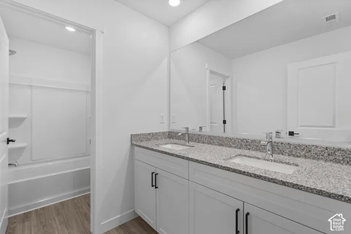 Full bath with double vanity, light wood-style flooring, recessed lighting, and shower / bath combination