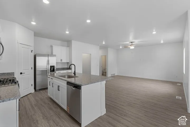 Kitchen featuring stainless steel appliances, white cabinets, a kitchen island with sink, recessed lighting, and light stone counters