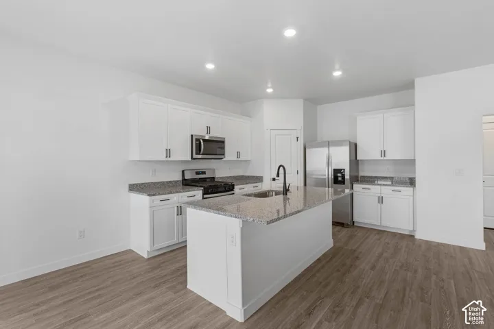 Kitchen with light wood finished floors, stainless steel appliances, light stone counters, white cabinetry, and recessed lighting