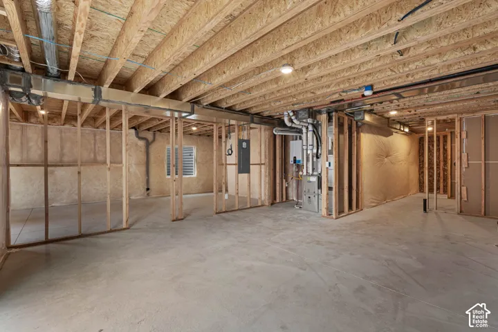Unfinished below grade area featuring heating unit, electric panel, and tankless water heater