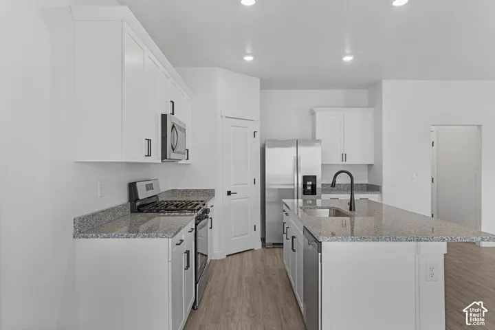 Kitchen with stainless steel appliances, light wood-style flooring, light stone countertops, white cabinetry, and recessed lighting