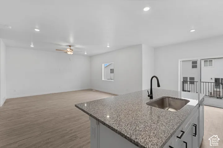 Kitchen featuring light stone counters, light wood finished floors, a kitchen island with sink, open floor plan, and recessed lighting