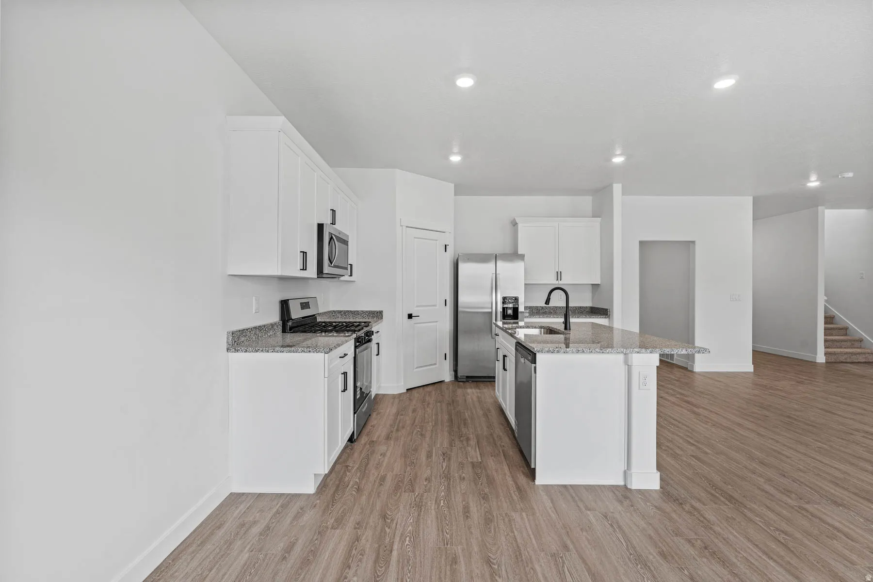 Kitchen featuring stainless steel appliances, white cabinetry, light stone counters, light wood-style floors, and a center island with sink