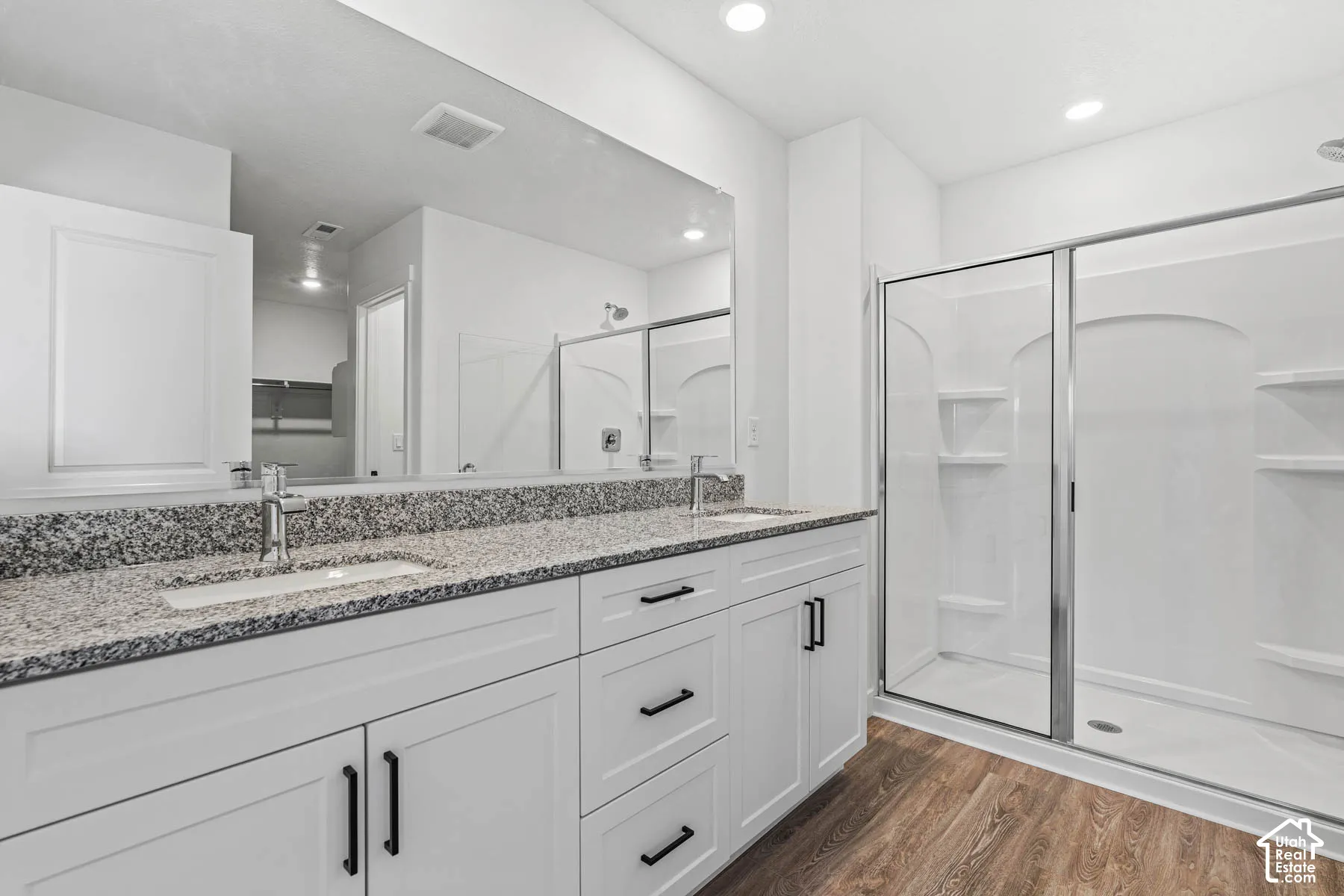 Full bath with double vanity, a shower stall, dark wood-type flooring, a walk in closet, and recessed lighting