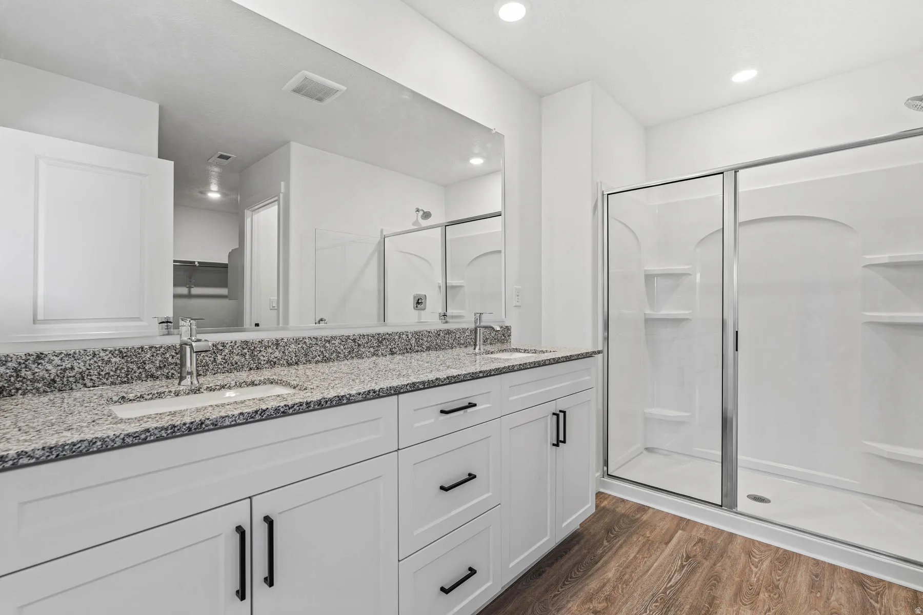 Full bath with double vanity, a shower stall, dark wood-type flooring, a walk in closet, and recessed lighting